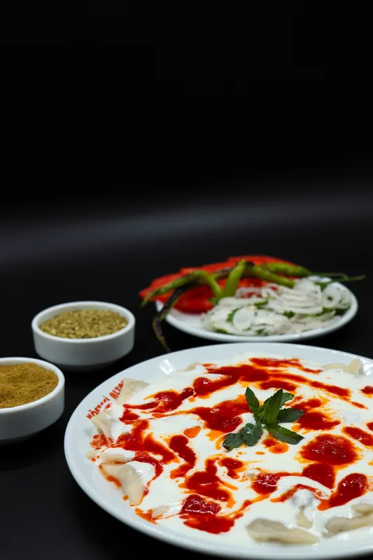 Koyu masada mantı tabağı, yanında yoğurt ve sos kâseleri