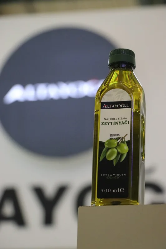 Fuar standında sergilenen zeytinyağı şişesi, arka planda bulanık marka logosu